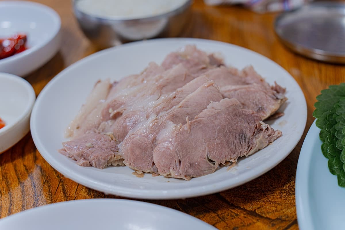 Thin slices of boiled meat arranged on a plate with dipping sauce
