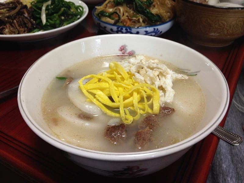 Sliced oval rice cakes in clear broth topped with egg ribbons and beef