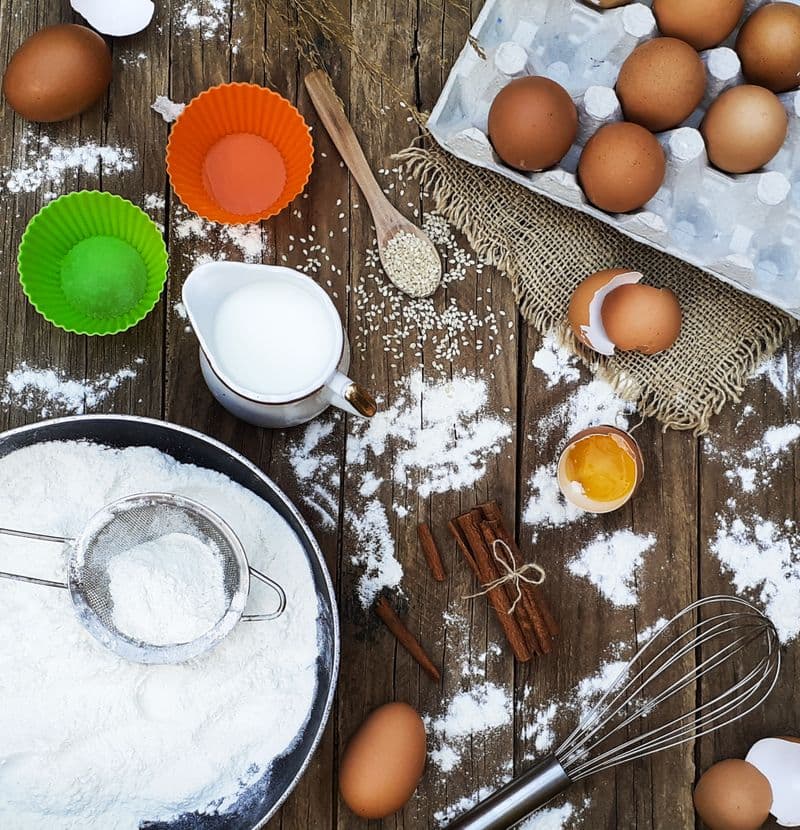 Flour, eggs, and baking tools arranged on a wooden table