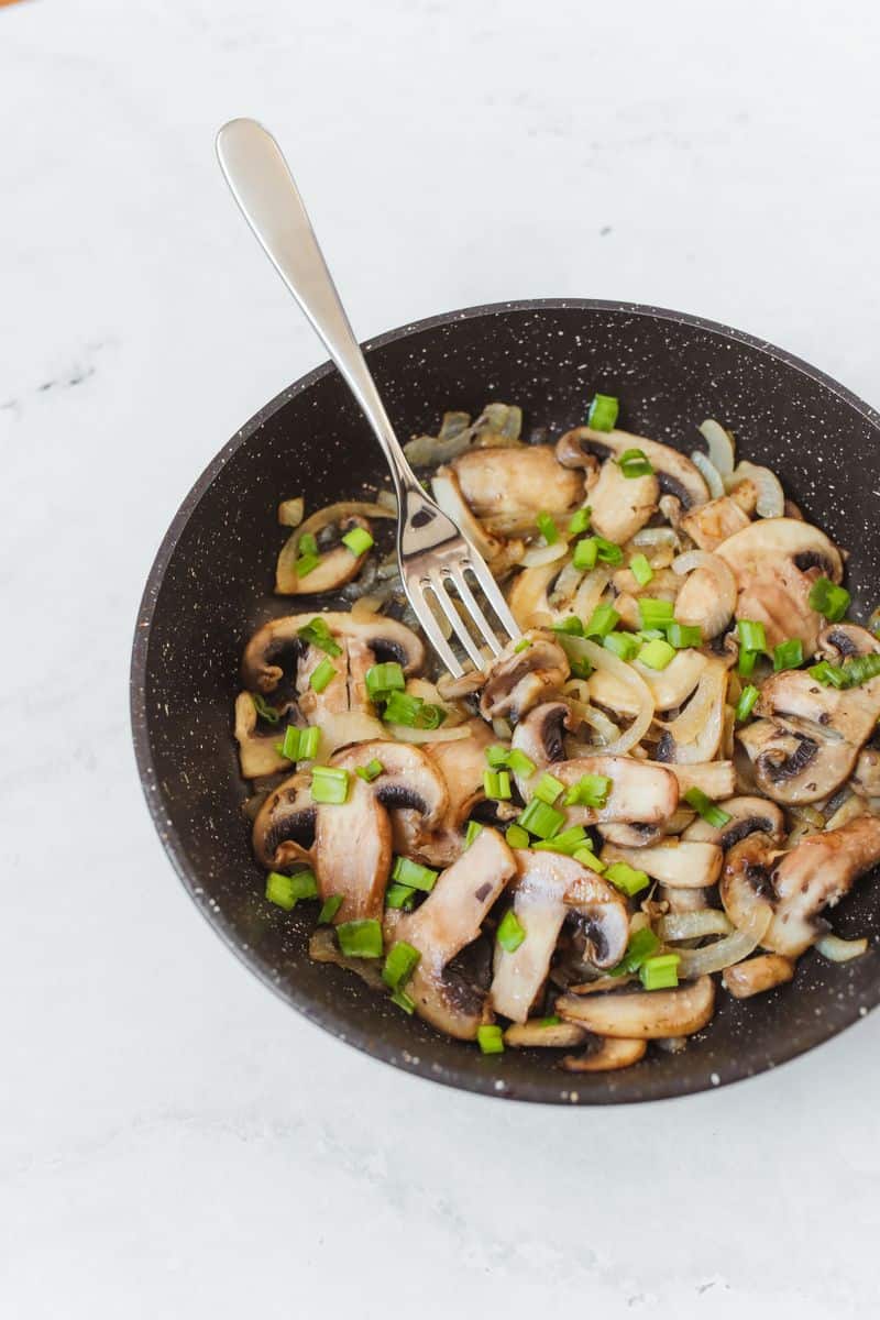 Sauteed mixed mushrooms and onions garnished with green onion in a bowl