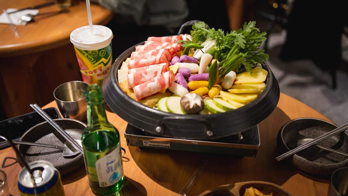A bubbling stew with sausage, spam, kimchi, and instant noodles in a shared pot