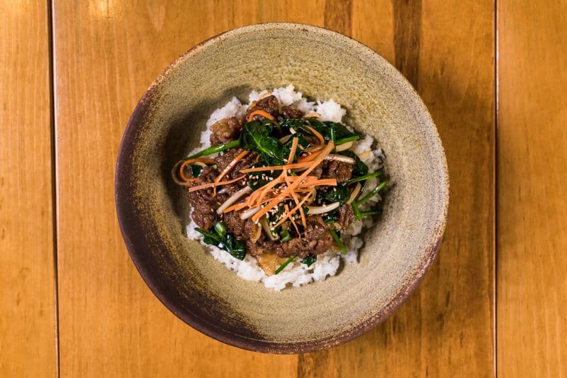 Glazed bulgogi beef with julienned carrots and spinach over white rice in a bowl