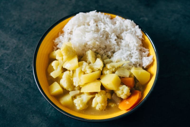 Yellow curry with potatoes and vegetables served beside white rice in a bowl