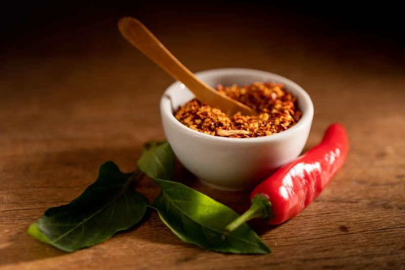 Coarse red chili flakes in a small white bowl with a fresh red chili alongside