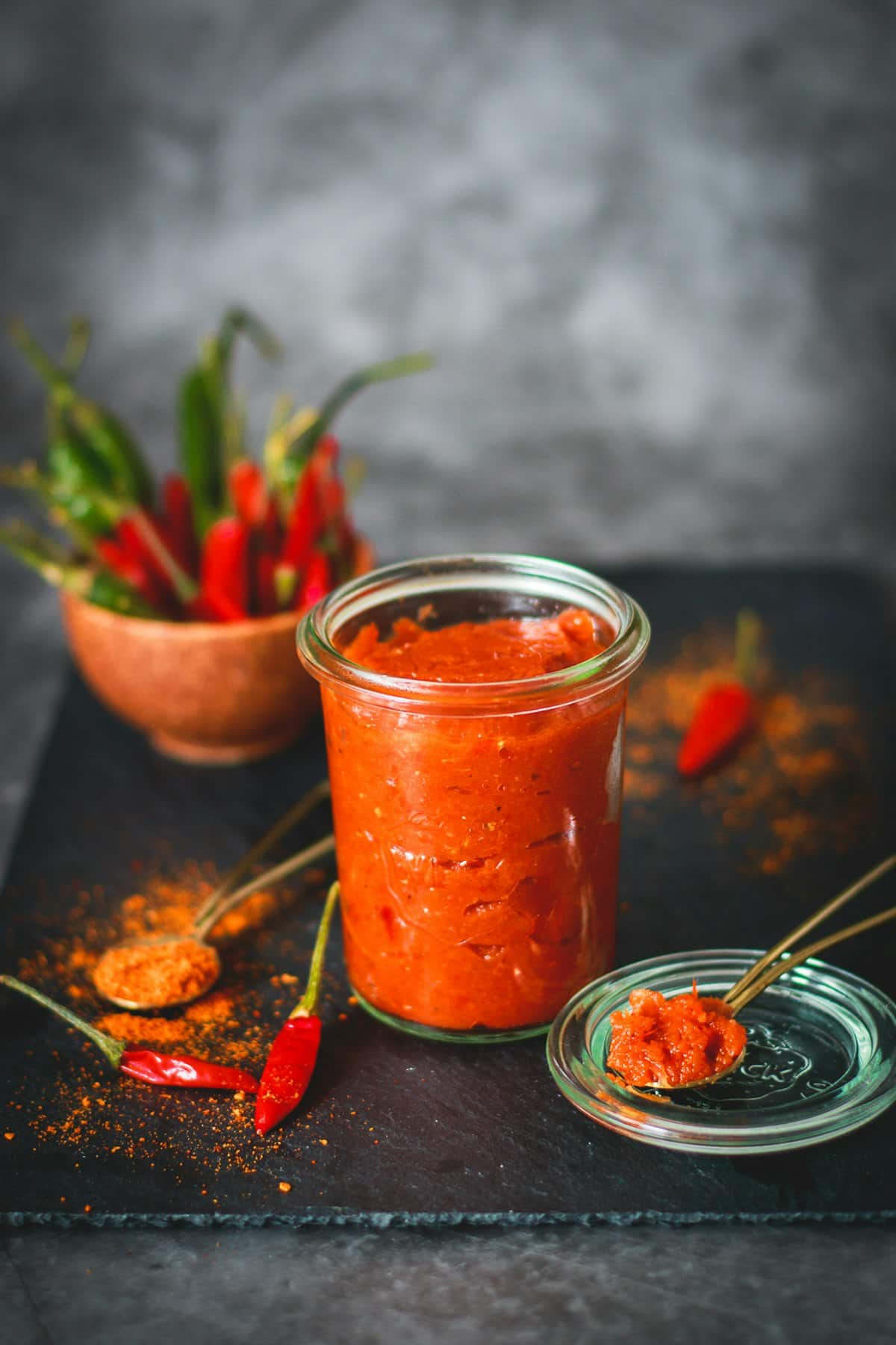 A jar of thick red gochujang paste with fresh chilies nearby