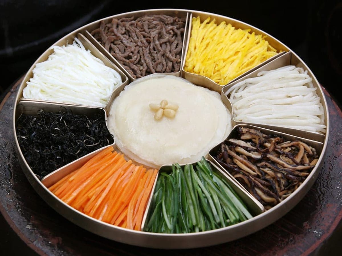 A round platter divided into nine sections filled with vegetables, egg and crepes