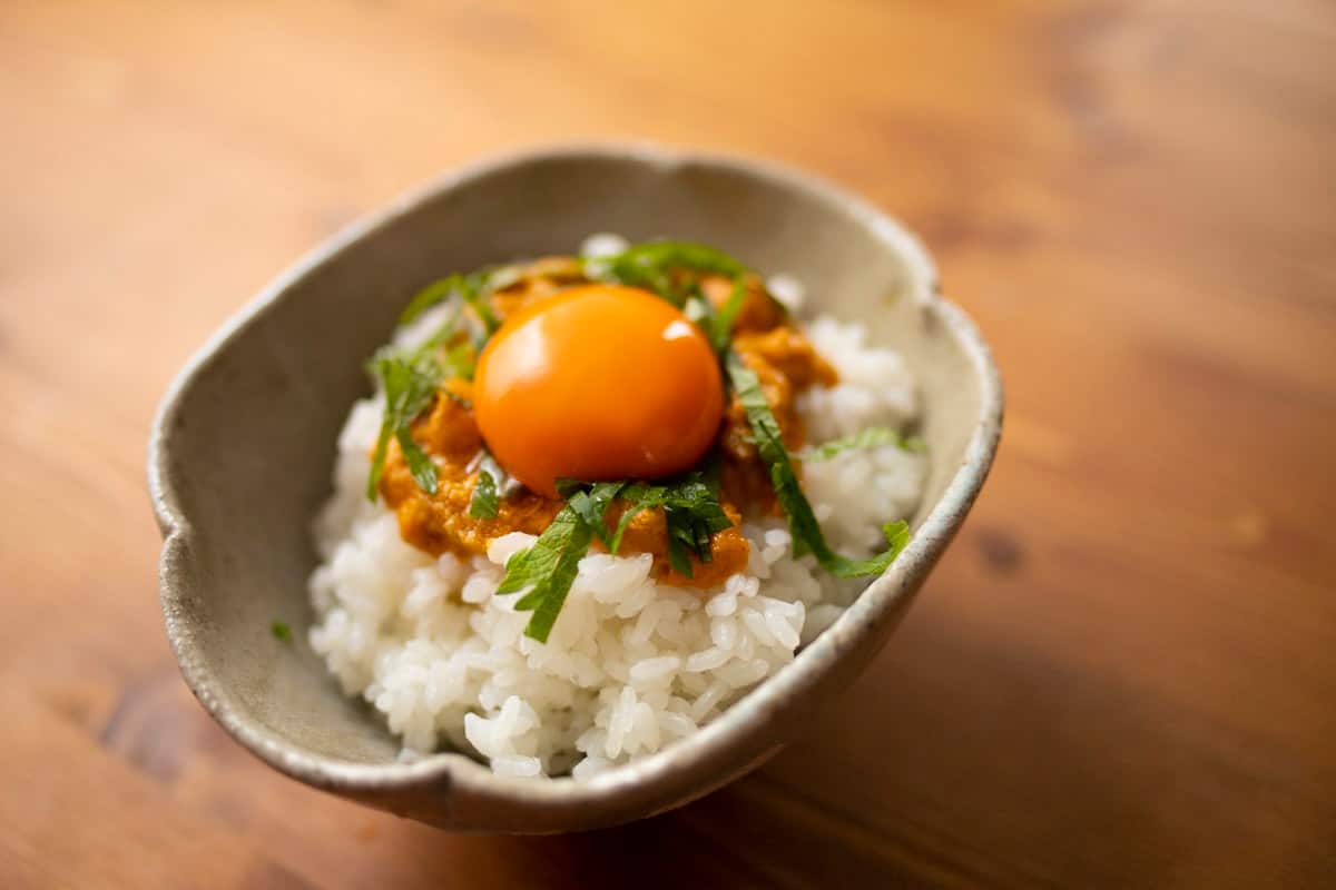 A raw egg yolk over warm rice with herbs, ready to be mixed