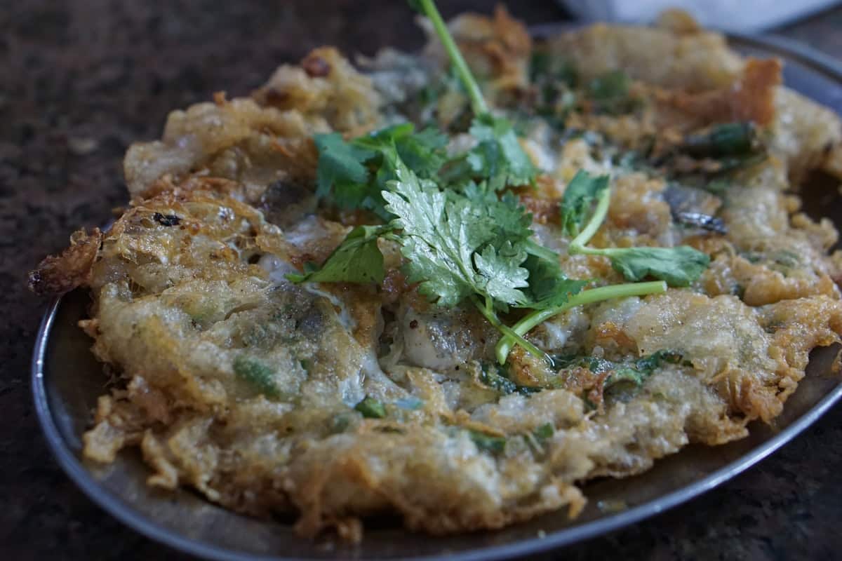 A savory scallion pancake with seafood and herbs on a plate