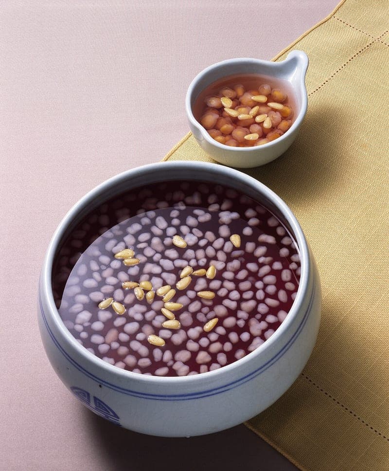 Magenta Korean punch in a ceramic bowl with small white rice pearls and floating pine nuts