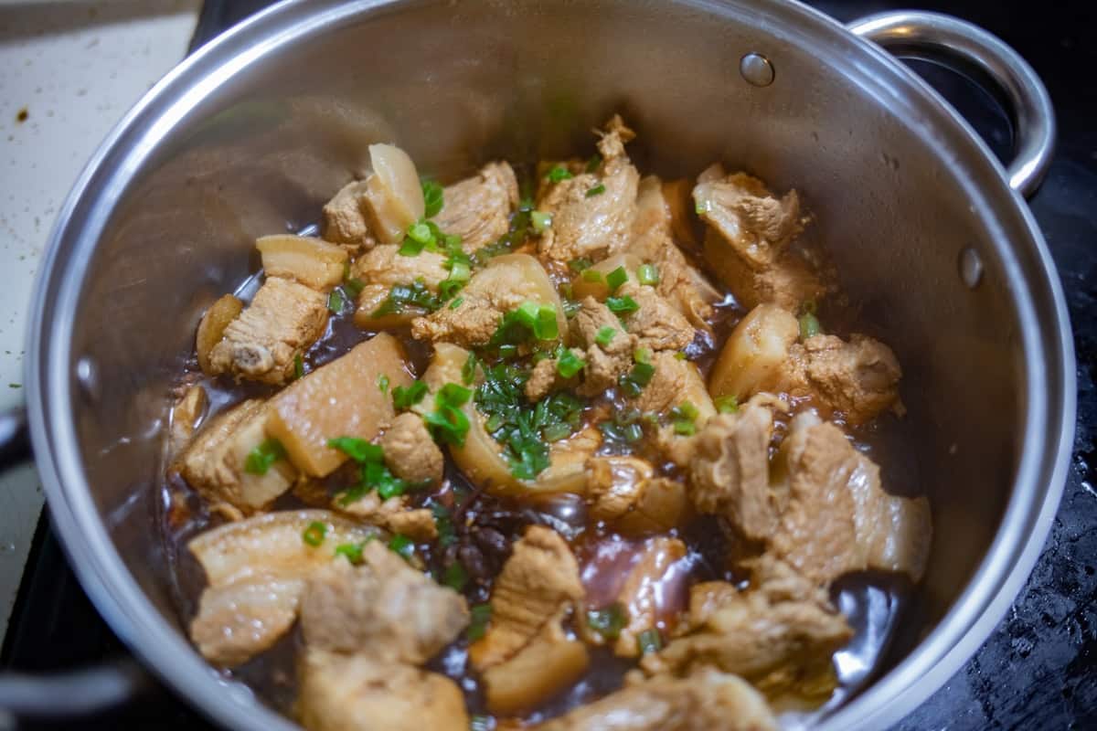 Chicken pieces braised in dark soy sauce with potato and scallion in a pot