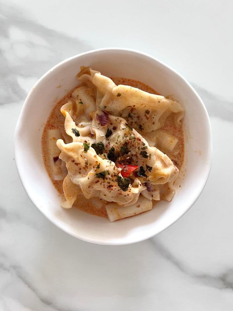 Dumplings floating in a reddish kimchi broth topped with herbs and chili