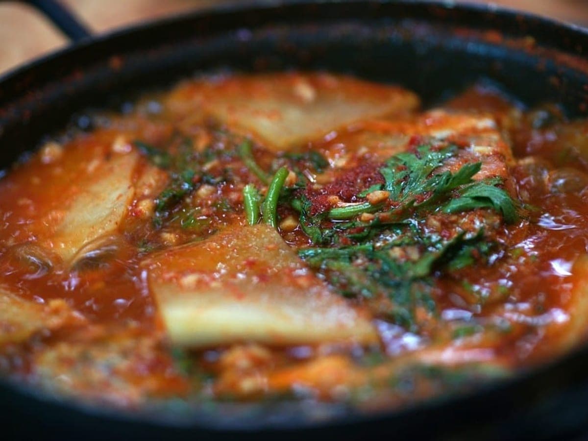 Bright red spicy fish stew with vegetables in a shallow pot