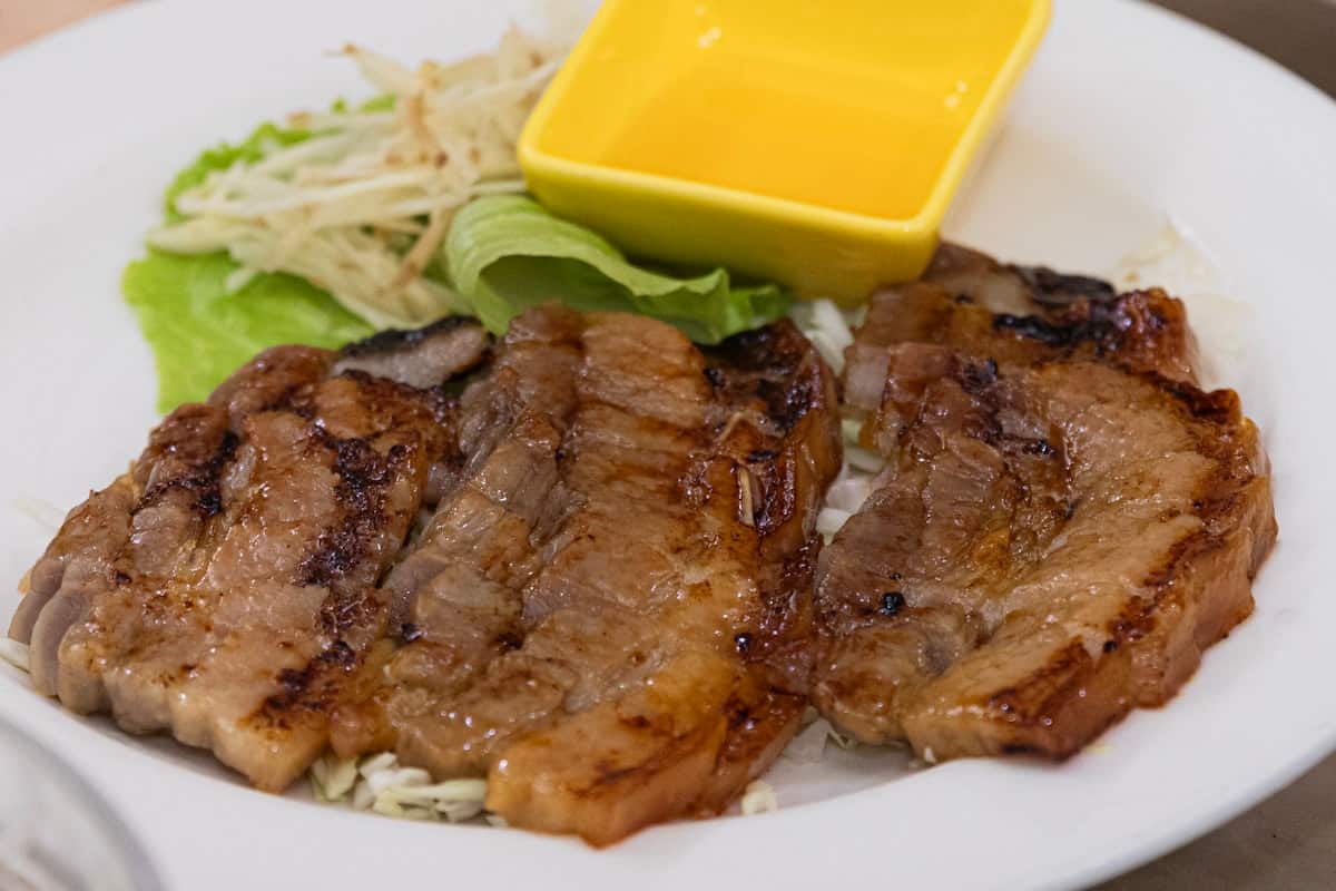 Grilled pork neck slices with char marks, served with lettuce and dipping sauce
