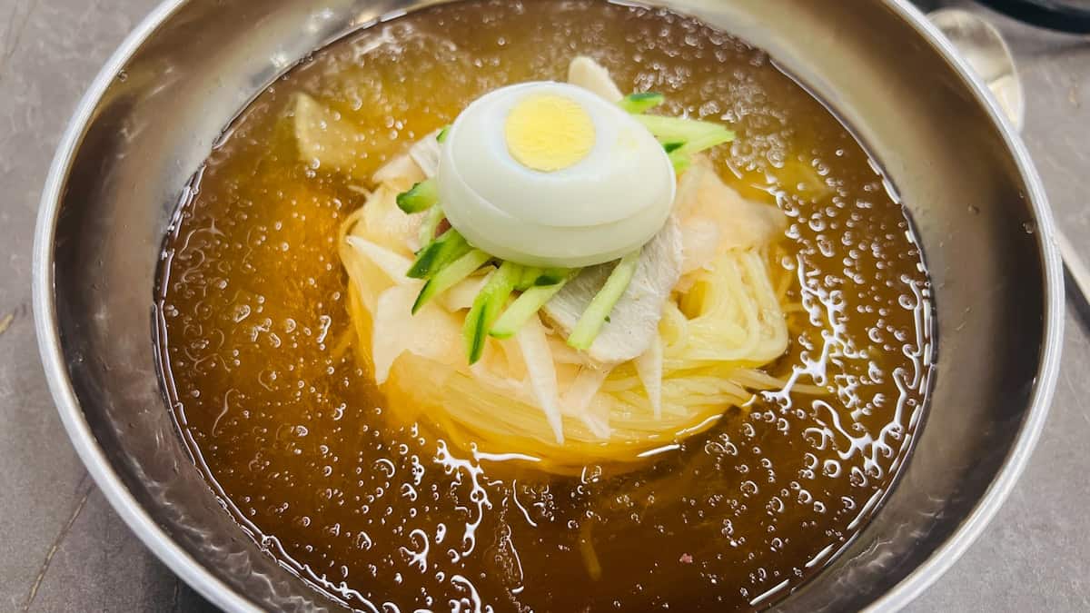 Cold Korean noodles in an icy amber broth topped with egg, cucumber, and radish
