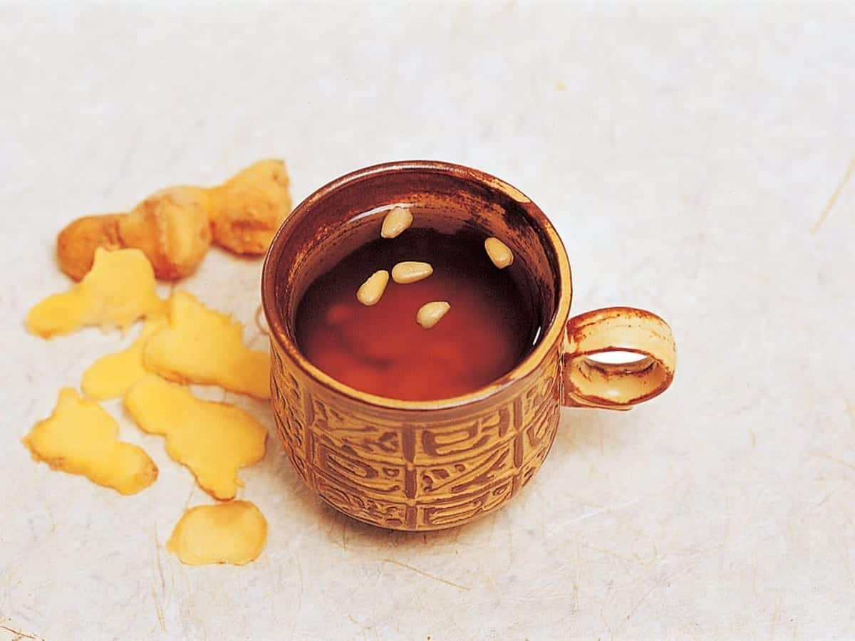 Amber ginger tea in a small cup with pine nuts floating on top