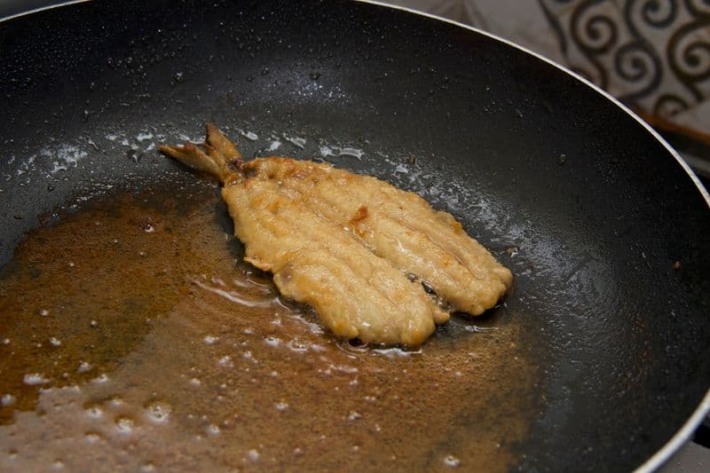 A golden egg-battered fish fillet frying in a pan