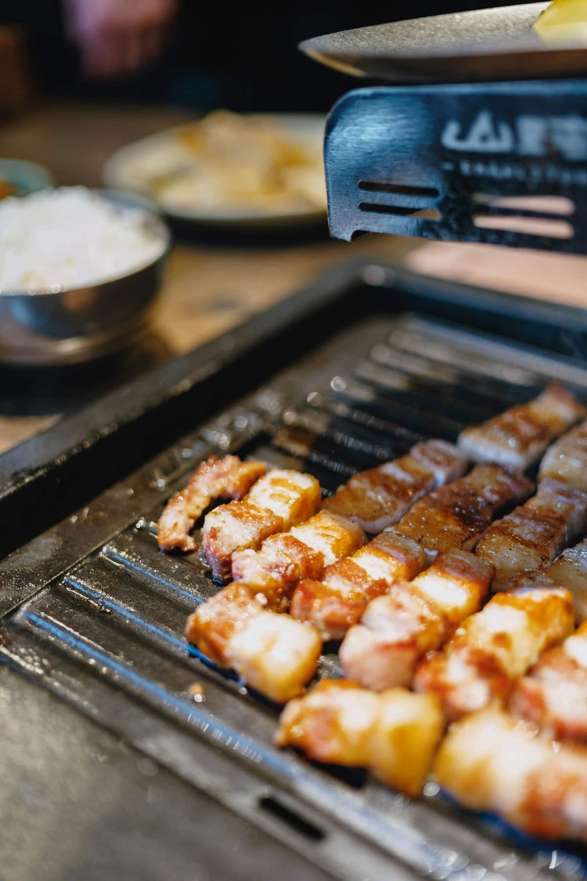 Strips of pork belly grilling on a Korean tabletop grill