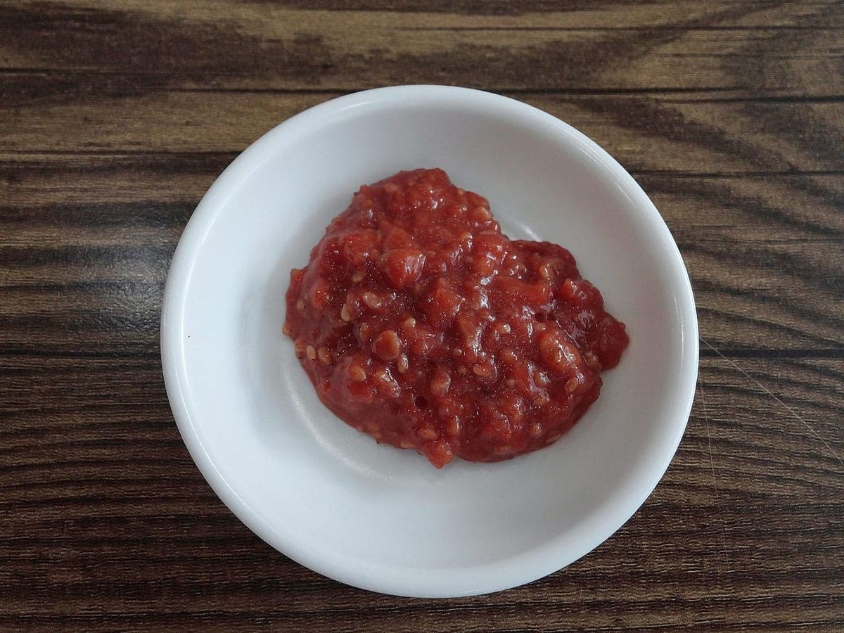 A small white dish of thick, chunky red-brown ssamjang on a wooden table