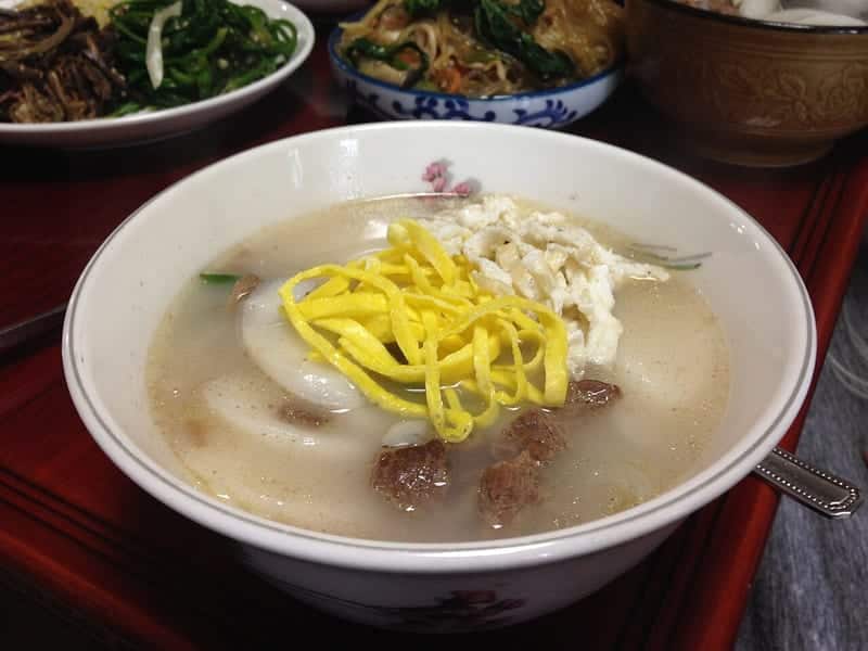 Sliced oval rice cakes in clear broth topped with egg ribbons and beef