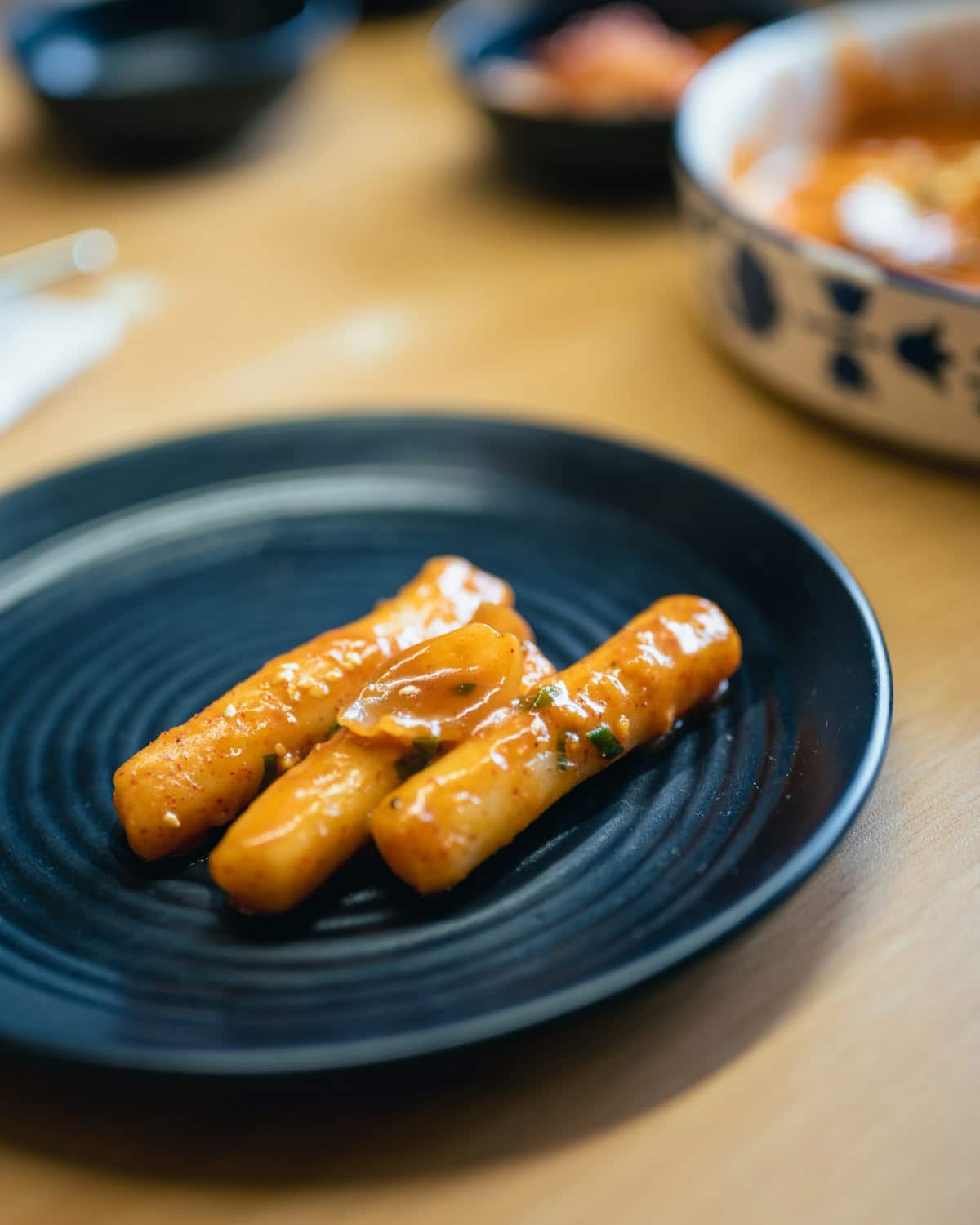 Glazed cylindrical rice cakes coated in spicy red sauce on a black plate